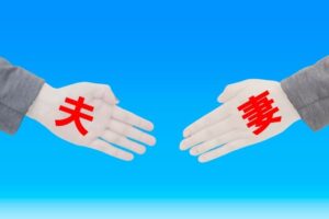 青背景で「夫」「妻」と赤字で書かれた人形で作られたそれぞれの手が握手をしようとしている